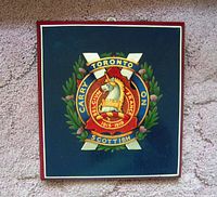 Photo of front view of the wooden plaque showing the enameled logo and inscription clearly.