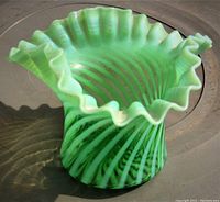 Front angled view of green Vaseline opalescent twist glass vase showing ruffled top and swirl pattern