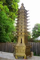 Full front view of the bronzed metal pagoda incense burner outdoors on a wooden ledge.