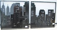 Two metal city skyline wall hangings in black paint with square window cutouts, shown from the front.