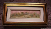 Framed oil painting showing a pink hued autumn landscape with trees and hills, artist signature visible.