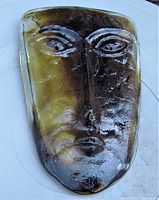 Front view of the amber and brown tinted Scandinavian art glass face sculpture showing carved features including eyes, nose, and lips.