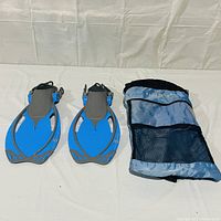 Wide shot of two blue Aqua Lung swimming flippers placed next to a blue and black mesh carrying case on a white background.