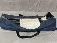 Blue soft fabric carrying case partially open, showing metal tubing framework and plastic parts inside along with assembly instructions.