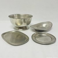 Four pewter items including a large bowl and three flat or shaped dishes