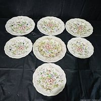 Six Royal Doulton Monmouth floral plates arranged on a black fabric background showing consistent floral patterns and scalloped edges.