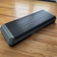 Side and top views of the black and gray exercise step platform showing textured surface and size.