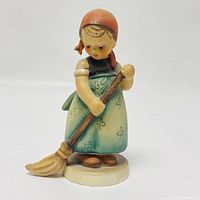Front view of Hummel girl figurine holding broom, showing details of her face, clothing, and broom