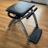 Side angled view of the Malibu Pilates stretcher showing padded seat, metal frame wrapped with protective tape, and footrest.