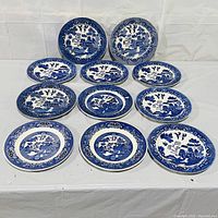 Set of 11 blue and white plates laid out on table showing front designs with Asian landscape motifs