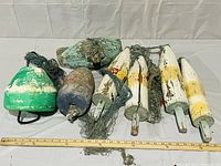 Photo showing seven vintage wooden buoys with fishing nets lying on a white surface, measuring approximately 24 inches in length with a ruler placed for scale.