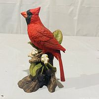 Side view of the red cardinal figurine perched on a detailed tree stump base with leaves and flowers.
