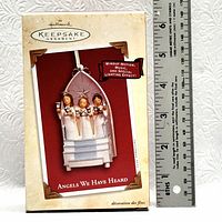 Front of the box for the Hallmark Keepsake Ornament Angels We Have Heard showing the ornament image and features including windup motion, music and special lighting effect alongside a ruler for scale.