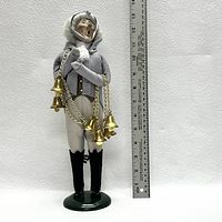 Front view of the Marley's Ghost figurine showing detailed clothes, face, and bells on chains, next to a ruler for scale.
