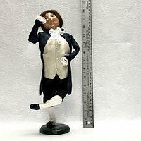 Mr Fezziwig figurine standing about 12 inches tall, posed dancing with one leg raised and one arm raised holding a glass, detailed period clothing painted in dark blue, cream, and white.