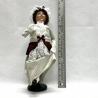 Mrs Fezziwig figurine standing next to a 16 inch ruler for scale, wearing cream and maroon period clothing with lace accents, approx. 13 inches tall.