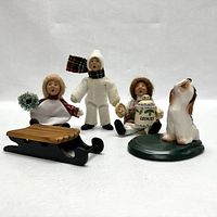 Front view of the four Byers' Choice figurines including three carolers and one dog, showing details of their winter clothing and accessories.