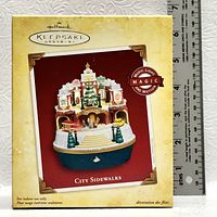 Box of Hallmark Keepsake Ornament City Sidewalks showing branding, photo of ornament, and feature badge 'Music Light Magic and Motion'.