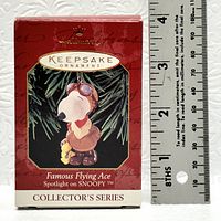 Photo of the boxed Hallmark Keepsake Ornament named 'Famous Flying Ace Spotlight on Snoopy' with a ruler to indicate size.