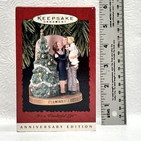 Photo of the ornament in its packaging, showing the design and box details with a ruler for scale.