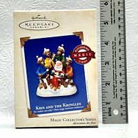 Box of Hallmark Keepsake Ornament 'Kris and the Kringles' showing product name, flickering magic light feature and size reference with ruler.