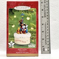 Photo showing the box front of the Merry Carolers Mickey and Co Windup Music and Movement Hallmark Keepsake Ornament from Christmas 2001, with a ruler for scale.