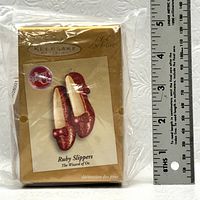 Photo of sealed original packaging of Ruby Slippers Keepsake Ornament showing branding, size reference with ruler, and club exclusive label.