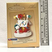 Front view of Hallmark Keepsake Ornament box featuring Snoopy with his decorated doghouse as a Christmas ornament. Box states 'Club Exclusive' and shows the Peanuts branding.