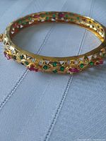 Close-up of one gold tone bangle showing lattice design with green, purple, and white stones