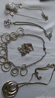 Various silver-tone chains and necklaces on white fabric, showing different styles including one with circular pendants and one with star pendant. Some clasps missing.