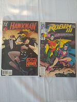 Photo showing two DC Comics comic books: Hawkman (Diana: Eyes of the Hawk) and Robin (Cry of the Huntress) with clear covers and visible titles.