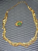 Gold tone chain necklace laid out in a circle showing detailed design and gold tone brooch with green stones in center