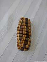 Photo of the handcrafted wooden beaded mini seashell bracelet with stacked rows of natural and dark brown wooden beads lying on white textured fabric.