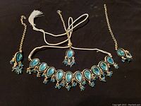 Full view of all three pieces of traditional Indian costume jewelry: necklace, headpiece, pair of earrings laid on a black fabric background.