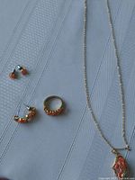 Full set of gold-tone peach stone costume jewelry on a grey textured background including a necklace with pendant, ring, stud earrings, and hoop earrings.