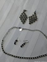 Full set showing both pairs of earrings and bracelet on a white textured fabric background.