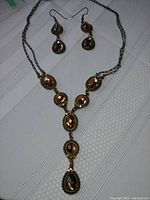 Full view of the chain necklace and matching earrings laid out on a white textured fabric background