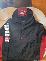 Full view of black and red Nike Air Jordan Jumpman jacket showing front with sleeve lettering and hood logo.
