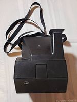 Front view of black Polaroid Sun 600 instant camera showing lens and flash area with attached shoulder strap.