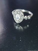 Ring with pear-shaped clear centerpiece stone surrounded by smaller clear stones, on a silver-tone band with round stones on either side.