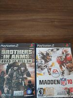 Front covers of Brothers in Arms: Road to Hill 30 and Madden NFL 10 PS2 game cases displayed on a wood surface.