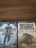 Photo of two PlayStation 2 video game cases: Call of Duty World at War Final Fronts and Brothers in Arms Earned in Blood side by side on a wood surface.