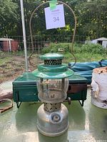 Photo of a weathered Coleman lantern with green painted top, clear glass globe, silver base, and carrying handle
