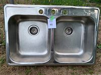 Photo of a double basin stainless steel kitchen sink with two drains and three faucet holes, showing surface dirt.