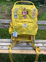 Yellow hunting backpack with aluminum frame and various sewn patches displayed on a wooden bench outdoors.