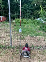 Full view of the Bauer hockey stick standing by the Cooper helmet with three hockey pucks stacked on top, all outdoors with a fenced garden background.