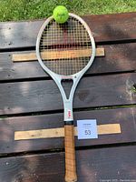 Full view of the Kneissl tennis racquet placed on wooden planks outdoors with a green tennis ball above the head of the racquet.