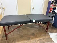 Full side view of portable massage table showing black padded surface and reddish wooden adjustable legs