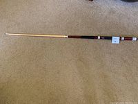 Full length of the cue stick laid on carpet showing the natural wood shaft and reddish-brown handle section.