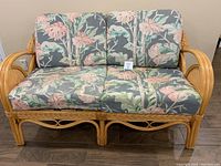 Front view of rattan loveseat with floral cushions depicting the seat and back cushions and rattan frame.